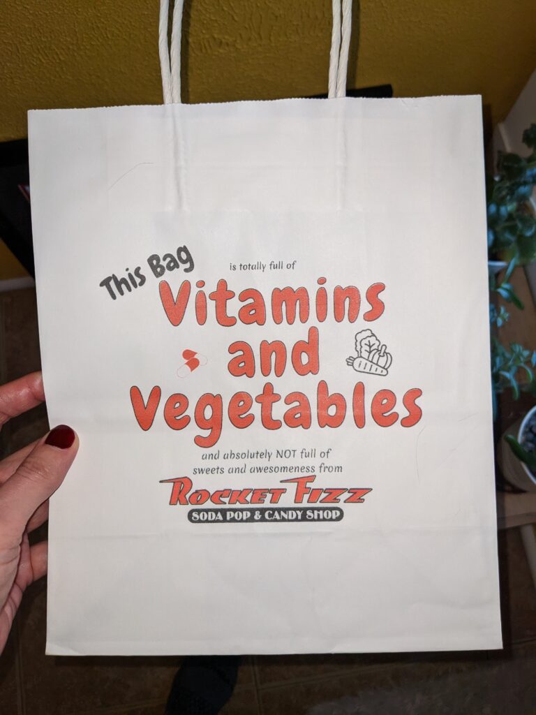 Bag has printing that says "This bag is totally full of vitamins and vegetables and absolutely NOT full of sweets and awesomeness from Rocket Fizz." 